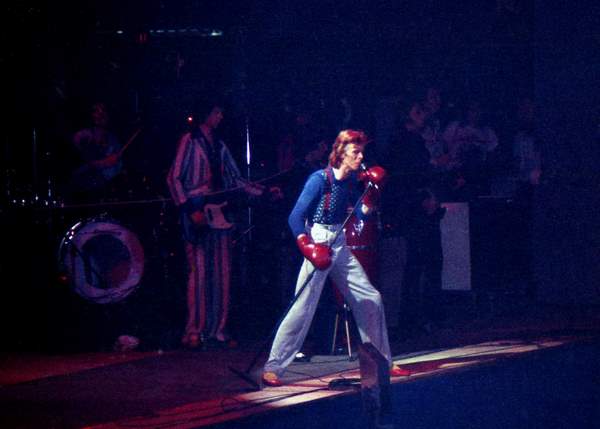 David Bowie performs at Charlotte Park Center, NC in 1974. wearing boxing gloves and high waisted pants.