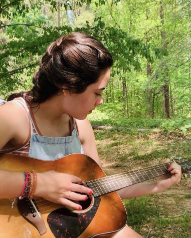 Lilly Chuman playing guitar in nature feeling the musical vibes of the earth.