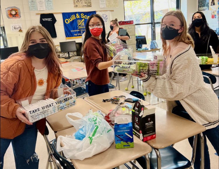 Students Jocelyn, Loren Liu, and Katie Little finish loading products into bins that are then hung up on walls in bathrooms around the schools. Some students raised concerns that adhesives might break easily, and the bins may fall. 
