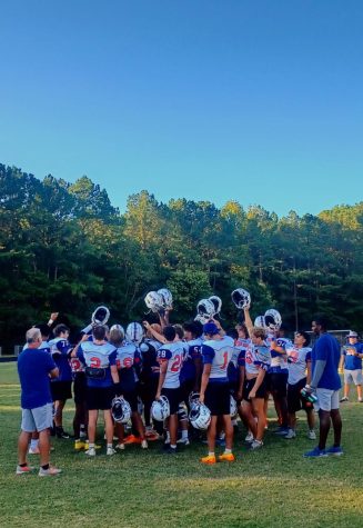 At the end of practice, Athens Drive football players raise their helmets after successfully putting in hard work for their upcoming game.