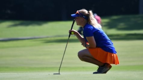 Susan McGraw crouched down on the golf field holding a putter.  She stares down the golf course ahead of her.
