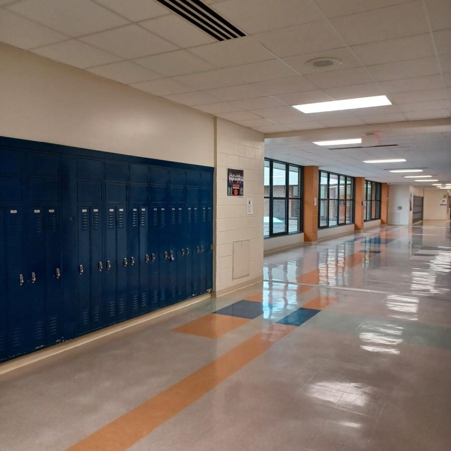 Bright ceiling lights reflect off of the newly waxed floor in one of the many hallways of Athens Drive High School. No students or teachers can be seen walking down the empty hallway. 