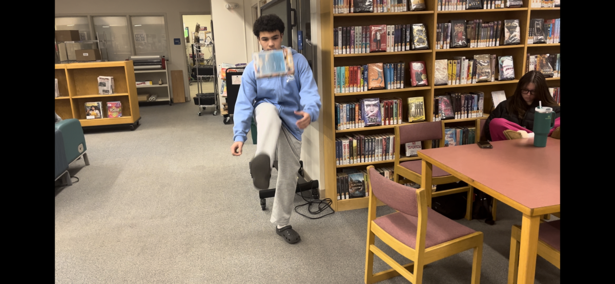 Adam Menouar showing off his skills by lifting up a book with his foot, and then catching it.