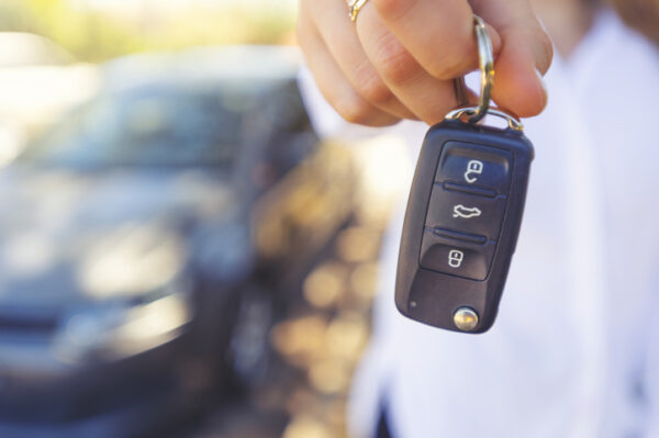 Car salesperson handing  over the new car keys. There is a new car behind her out of focus. 