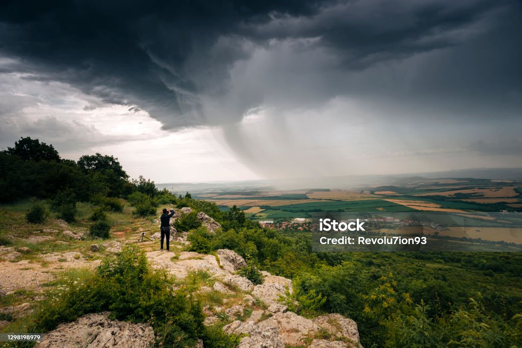 Man standing on the edge of the cliff and photograph a nice structured storm clouds in the summer fields