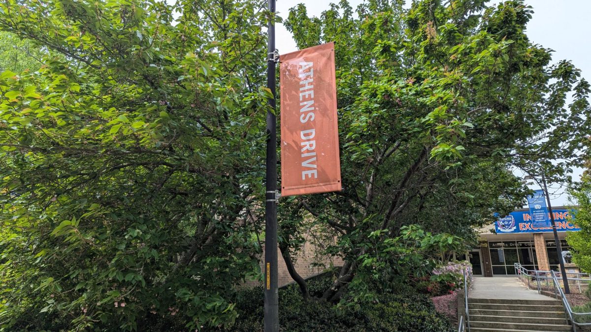 An orange banner with the words Athens Drive written on it. The banner flies in front of some trees.