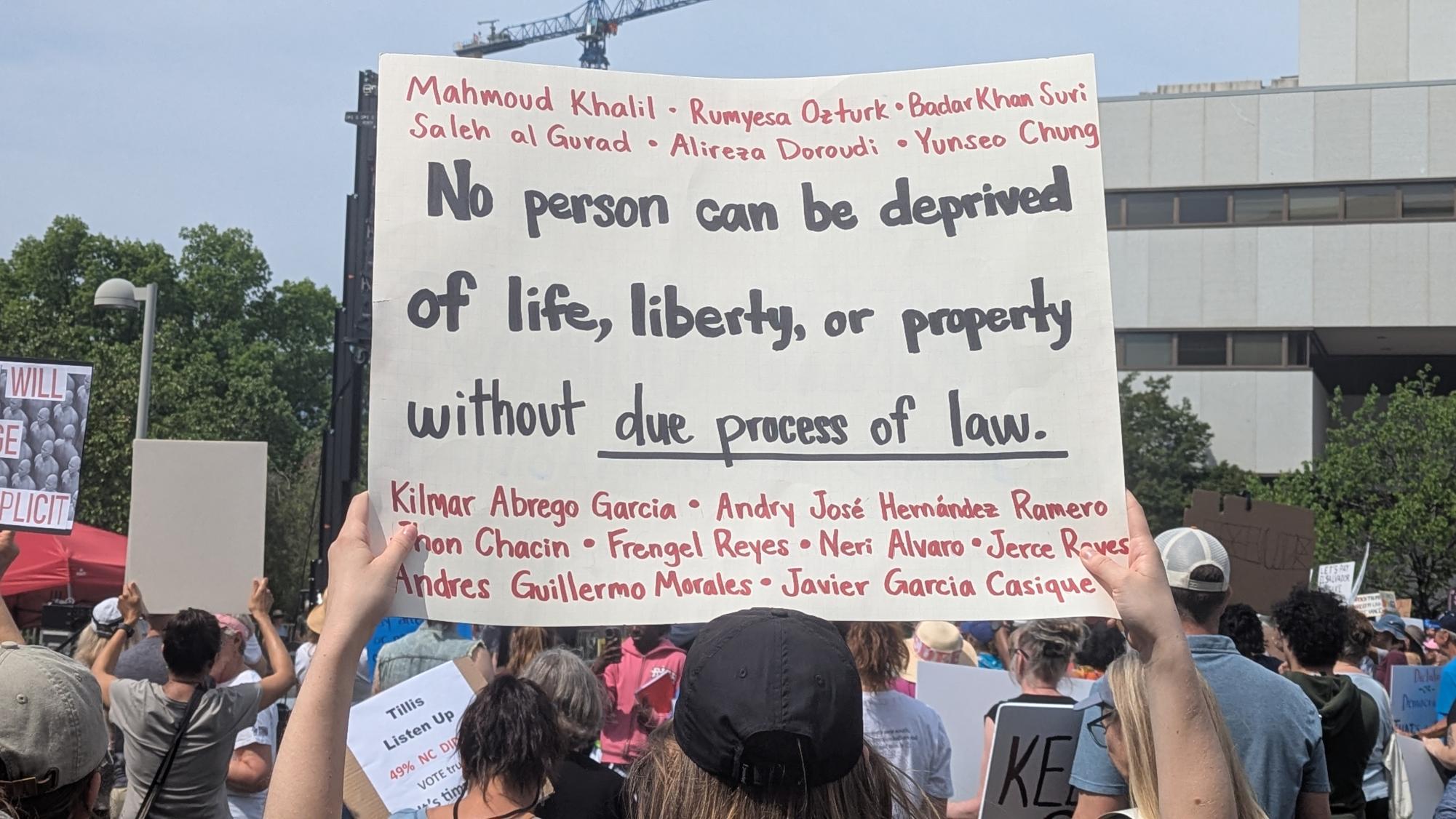 A protester at the Raleigh April 19th "Forward Together" protest. They are carrying a sign with the Constitution's due process clause, & the names of various people who have been detained or deported without due process 