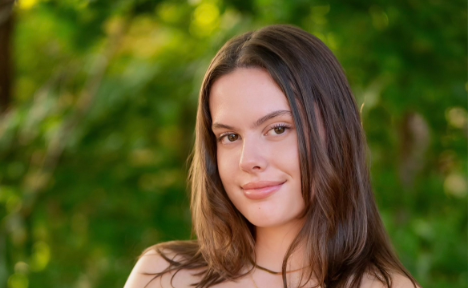 Grace Woodall posing for her Senior photos. She is outside in front of a green background.