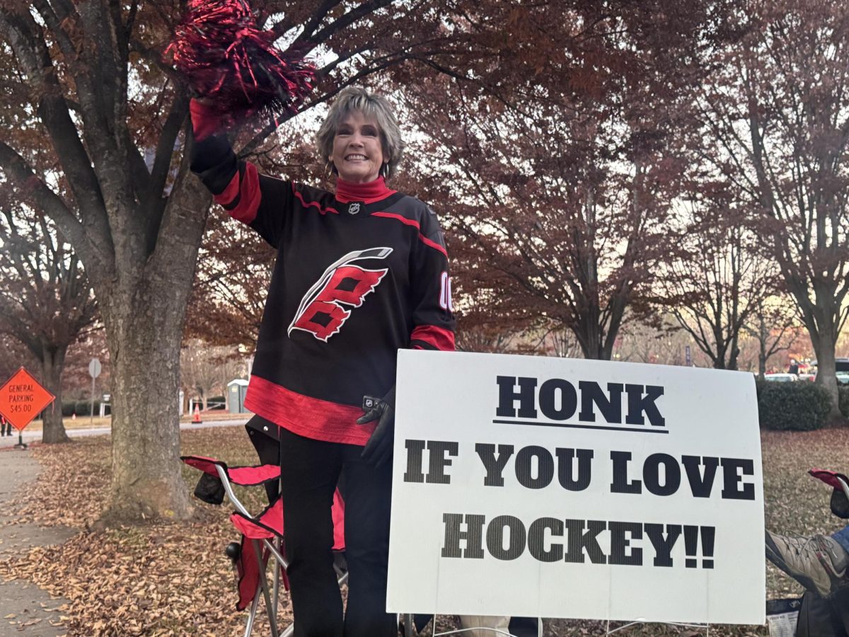 Hurricanes fan waves her red and black pom-pom in front of her sign that is meant to excite fans as they drive into the Lenovo Center parking lot. She does this before every game in order to spread some cheer to other Caniacs. 