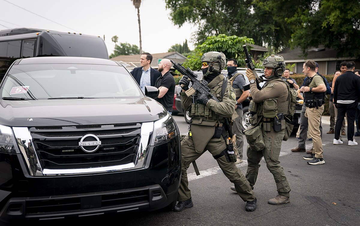 US Immigration and Customs Enforcement (ICE) conducting an Enforcement and Removal Operation (ERO) in Los Angeles, June 12, 2025. Agents are armed with military vests and guns, and wearing masks. Image is in the public domain, taken by Tia Dufour from the Department of Homeland Security.