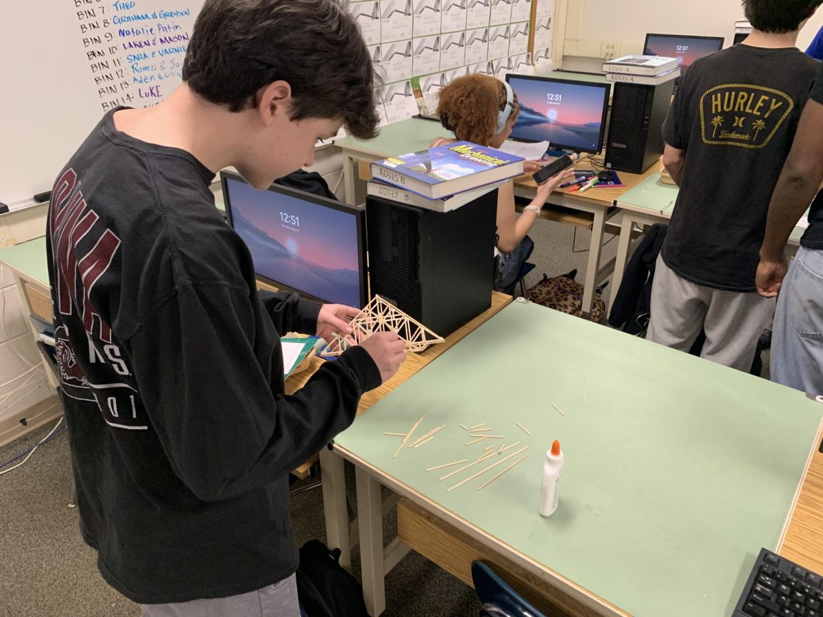 Elliott Marshall working on his bridge design so it is ready to test. The bridge is made out of balsa wood and put together with glue.