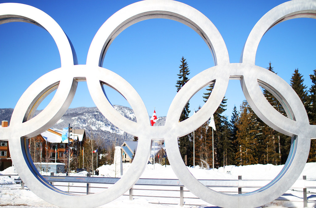 The Olympic rings standing in front of the snowy background of the Winter Olympics. While many sports catch the attention of viewers, ice hockey is consistently a top viewed event. (Whistler Olympic Rings by profernity is licensed under CC by 4.0)